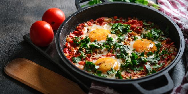 Baked Eggs with Tomatoes, Red Bell Pepper & Garlic in a iron pan on a dark background.