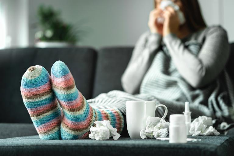 a young woman in comfy socks with a mug, nasal spray, and used tissues