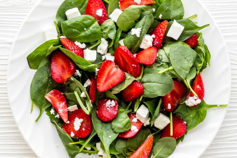 a plate of spinach, crumbled feta, and sliced strawberries